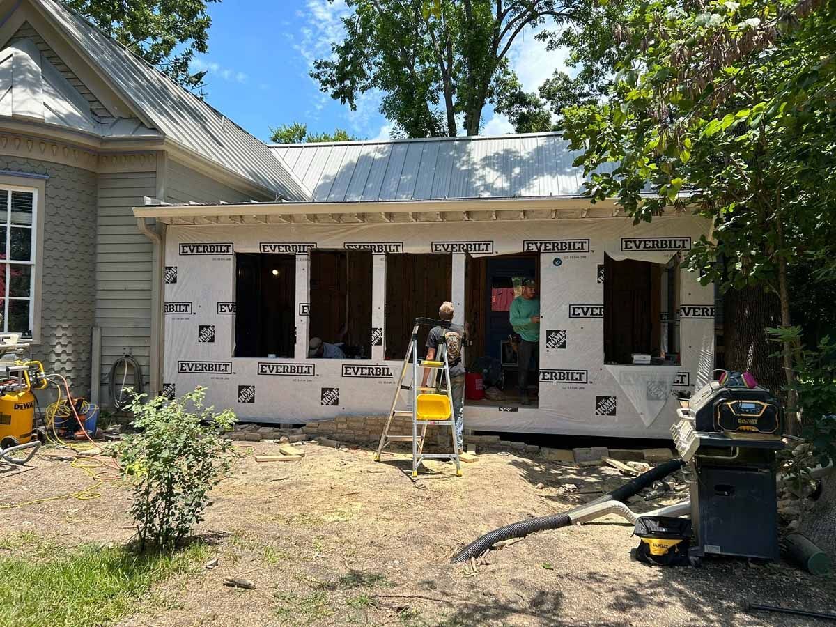 Exterior view of a building under construction, featuring windows, black wrap, and construction materials.