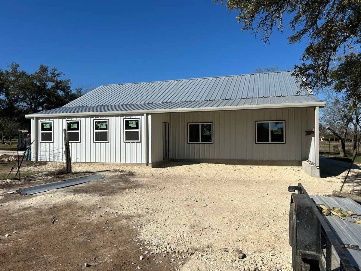 A one-story building under construction with a metal roof and white siding. Gravel in the foreground.