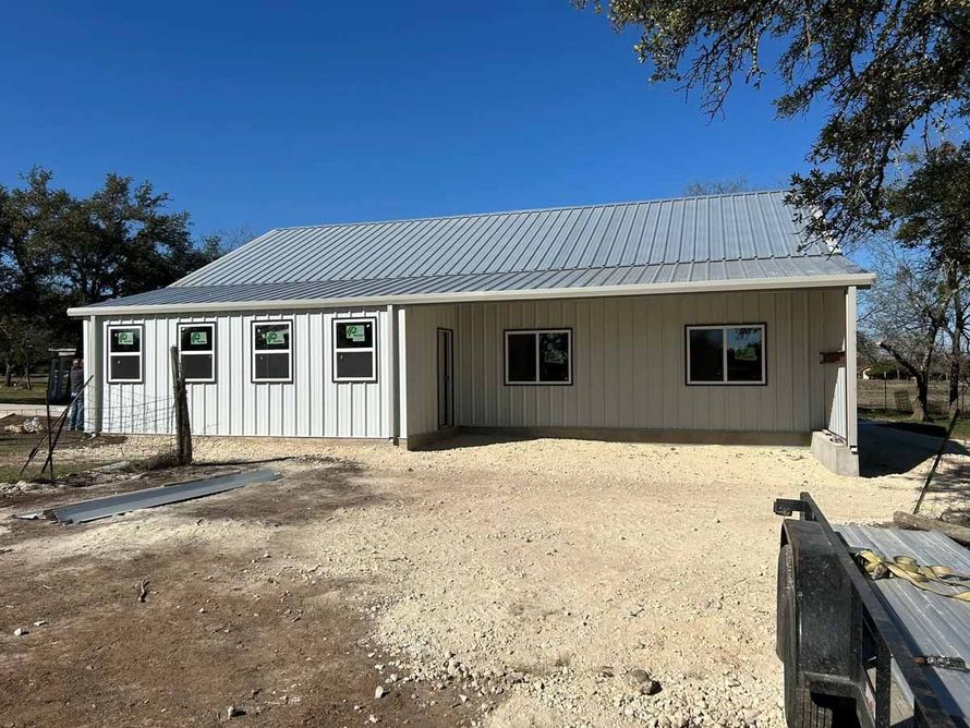 A one-story building under construction with a metal roof and white siding. Gravel in the foreground.