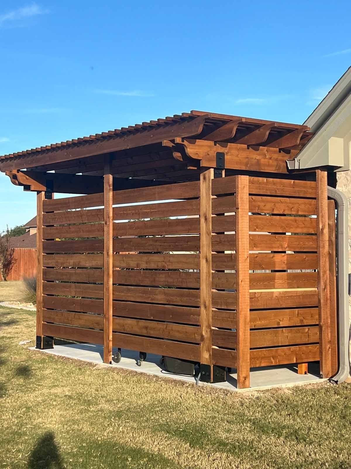 Wooden outdoor storage structure with a slatted privacy screen and pergola roof, on a lawn.