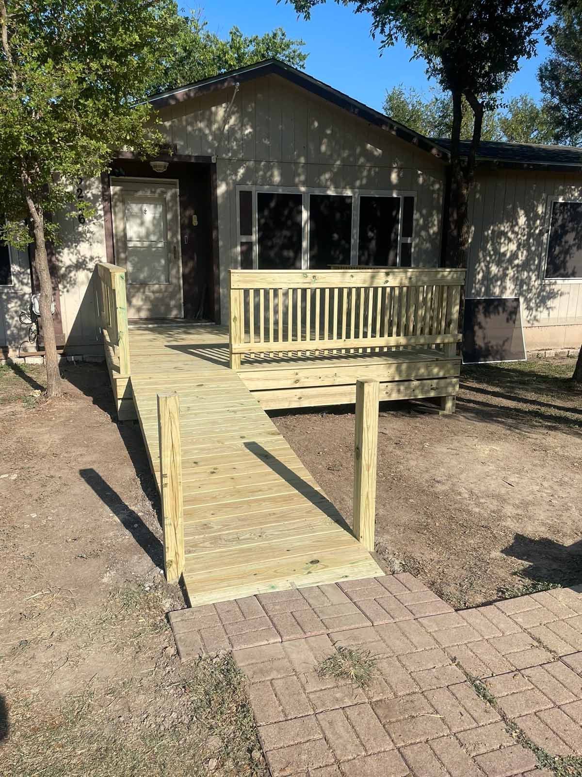 Wooden ramp leading to a small house with a porch and brick pathway.