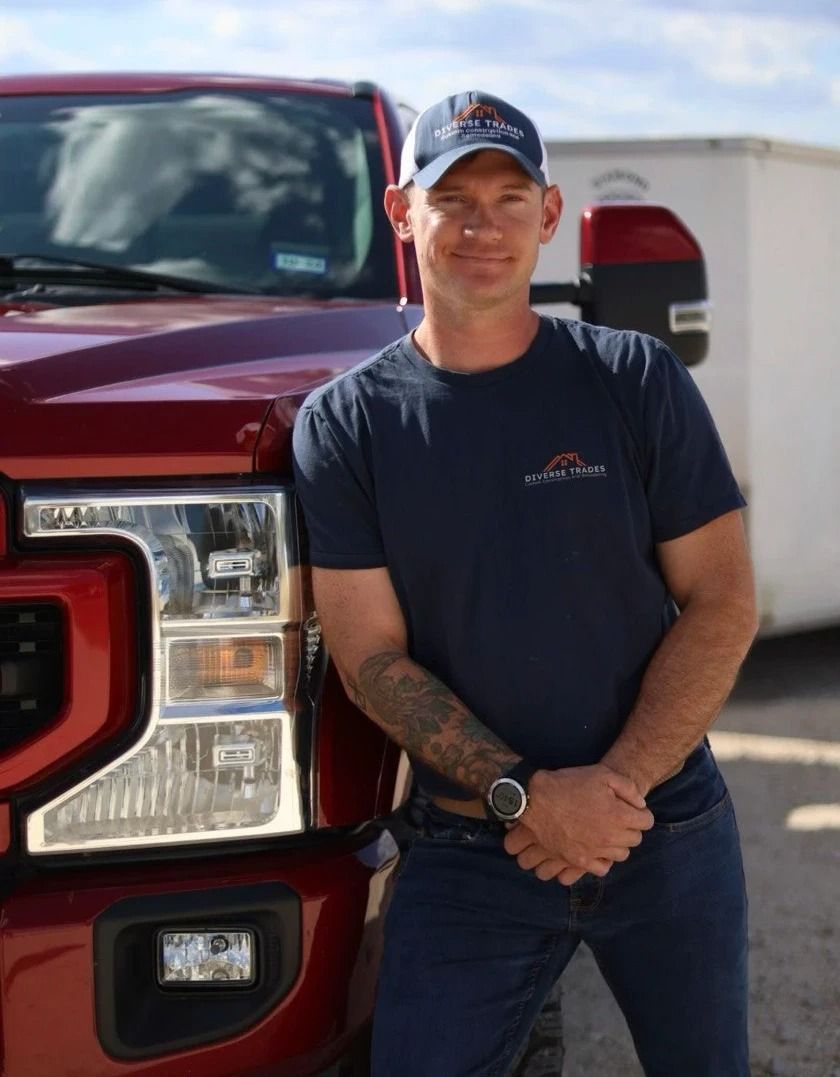 Man in a blue shirt and baseball cap, leaning against a red pickup truck, smiling.
