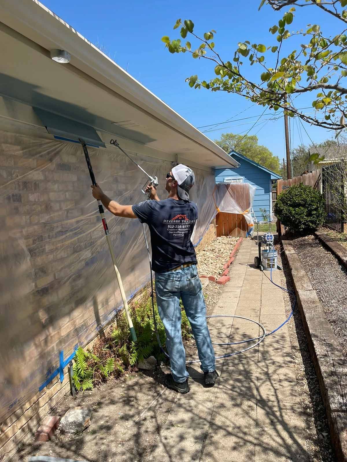 Person painting a brick wall blue with a spray gun; outdoor setting.