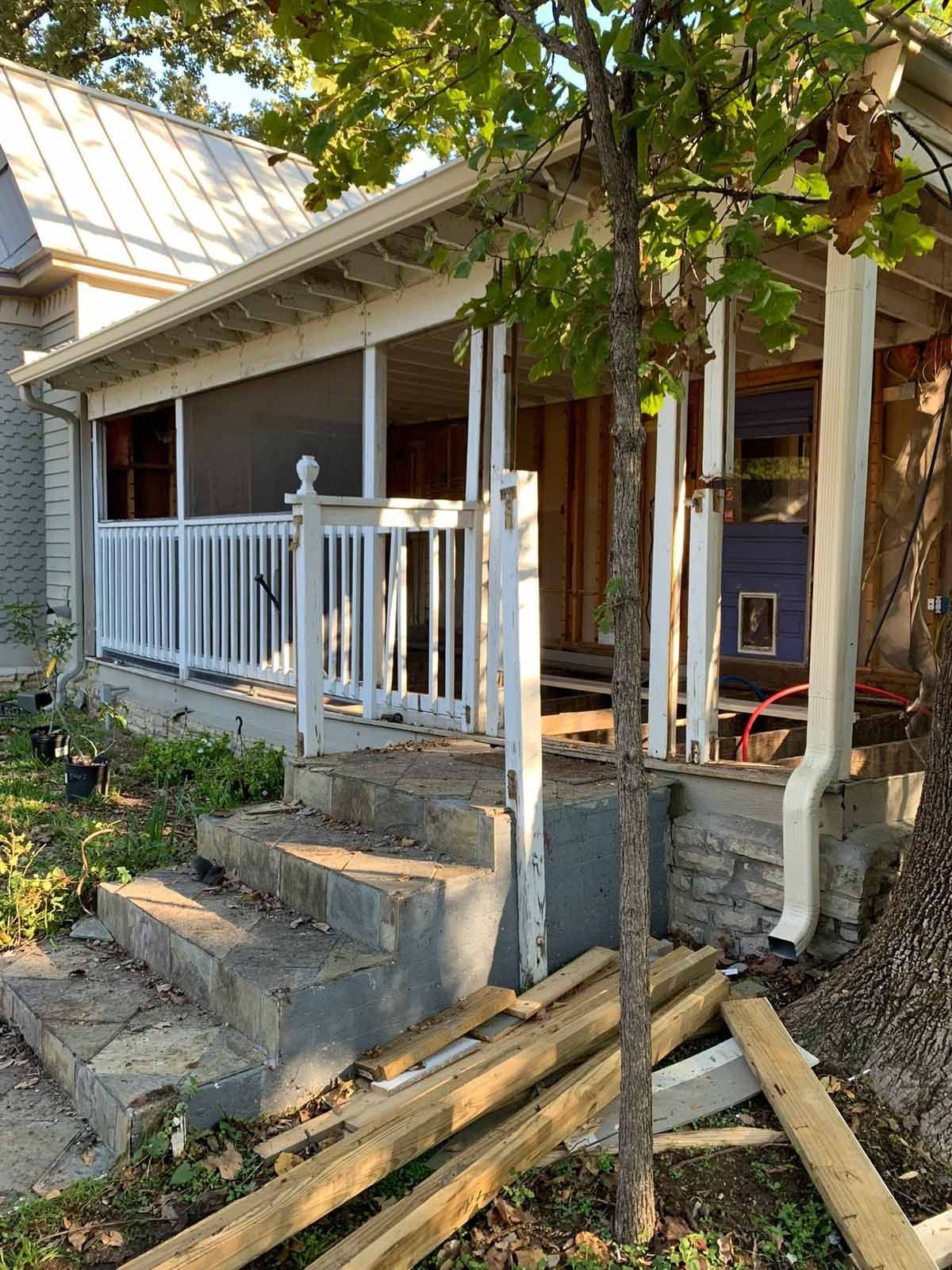 House with porch under construction; concrete steps, white railings, exposed wood and doorway.