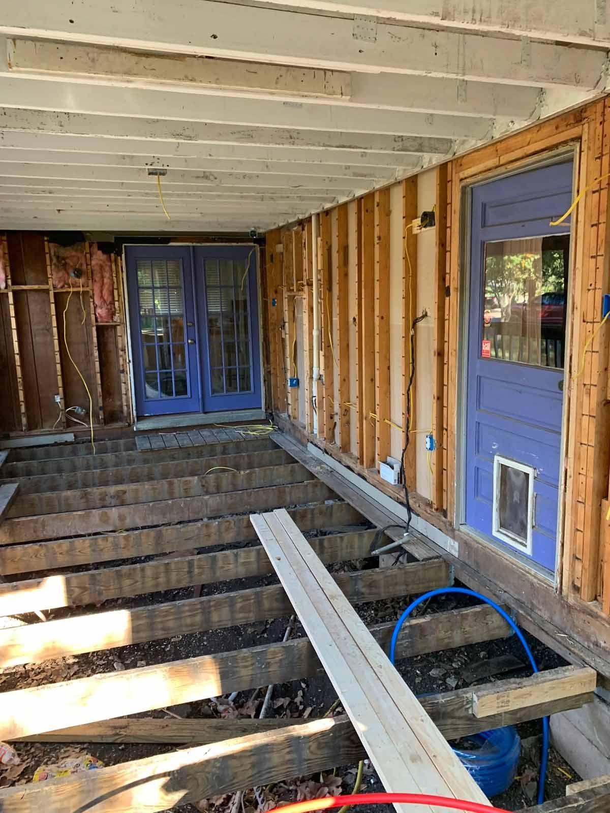 Porch under construction, with exposed framing, blue doors, and wooden beams.