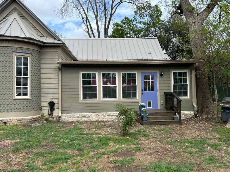 Tan house with a light blue door and white-framed windows, porch with wooden steps, and a tree to the right.