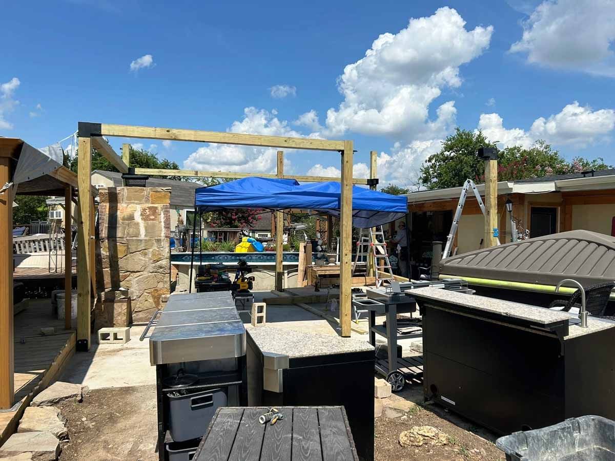 Construction of a wooden structure. Blue tarp, various equipment, and blue sky visible.