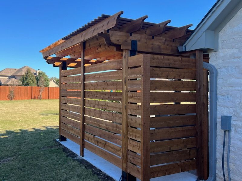 Wooden outdoor shower stall with pergola roof, brown stain, concrete base, and siding on the right.