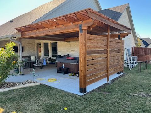 Wooden pergola structure with horizontal privacy screen over a patio, hot tub visible.