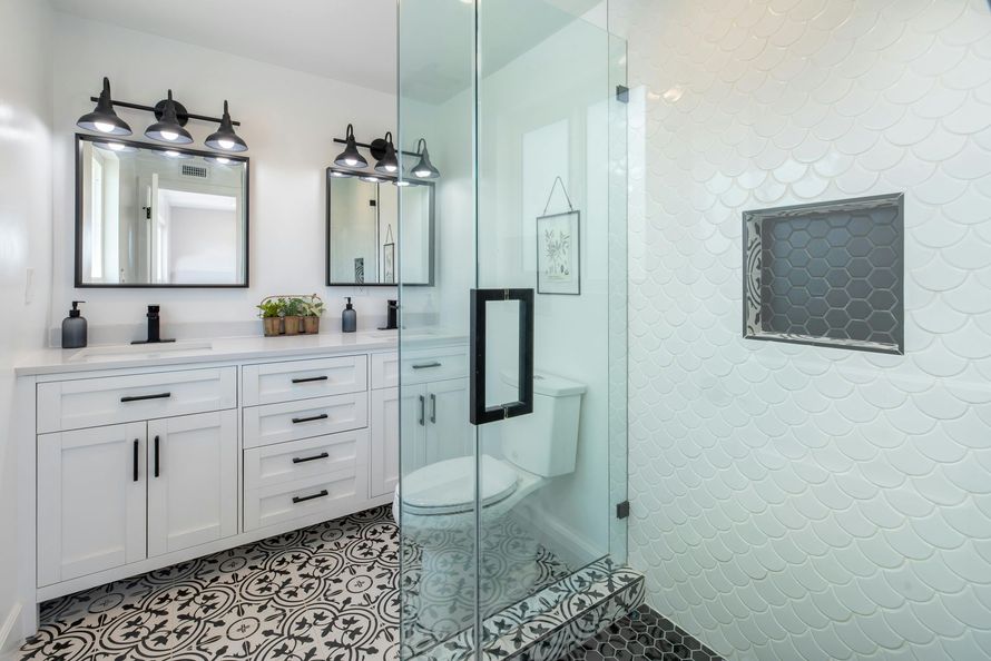 Modern white and black bathroom with glass shower, patterned floor, and dual vanity.