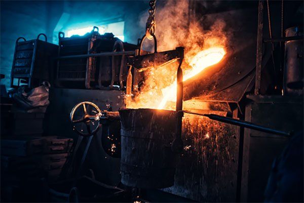 A bucket of molten metal is being poured into a ladle in a factory.
