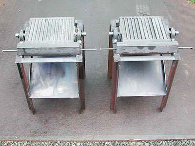 Two metal grills are sitting next to each other on a gravel road.