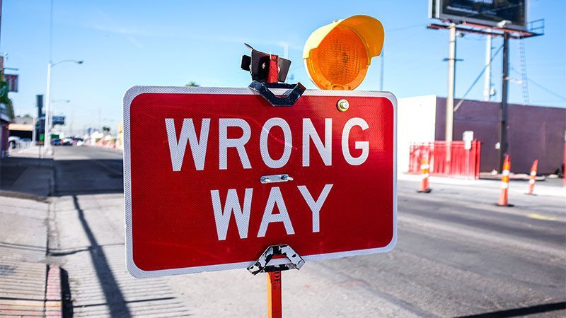 A red sign that says wrong way is on the side of a road.