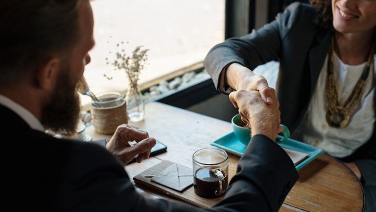 A man and a woman are shaking hands at a table.