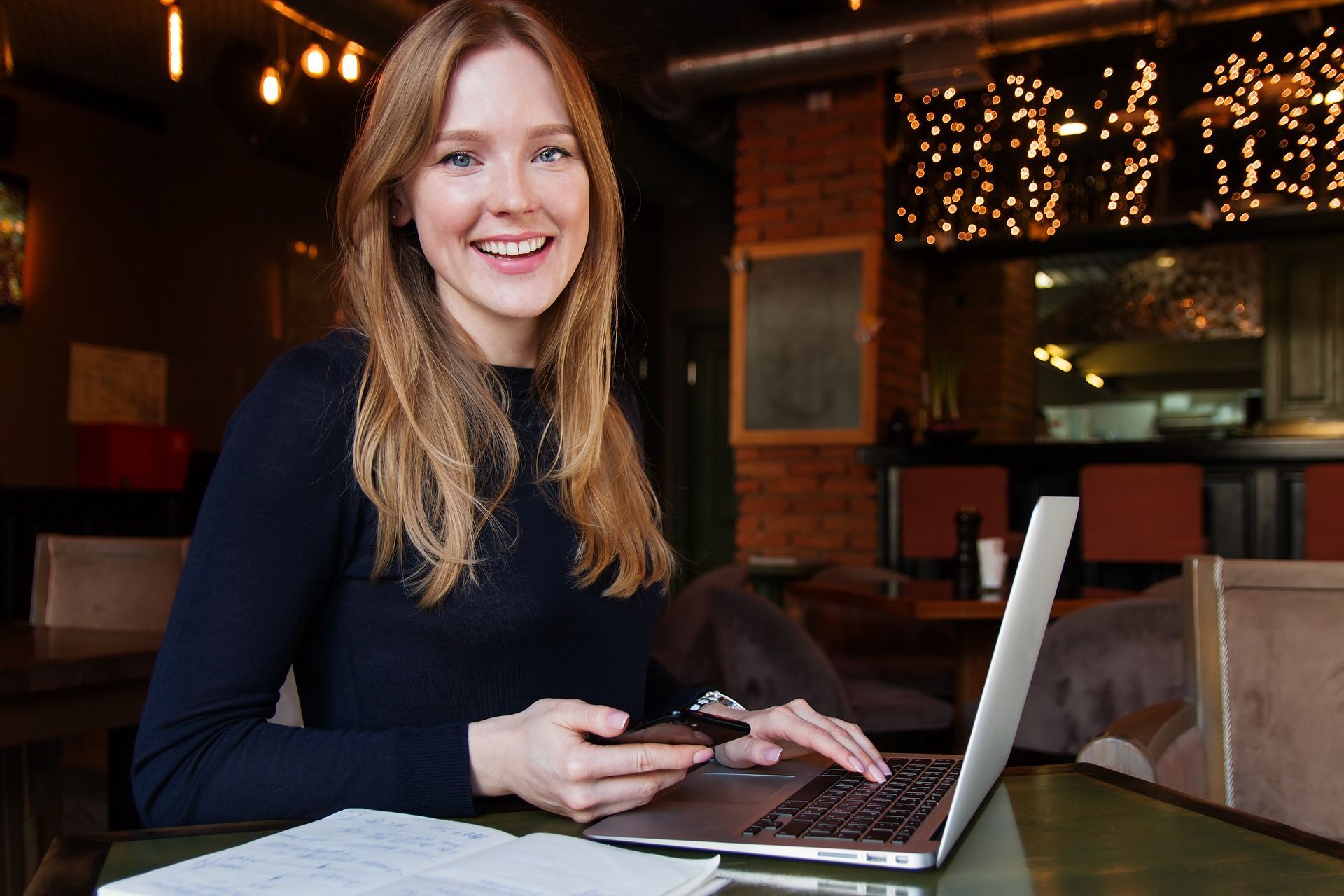 A woman is sitting at a table with a laptop and a cell phone.
