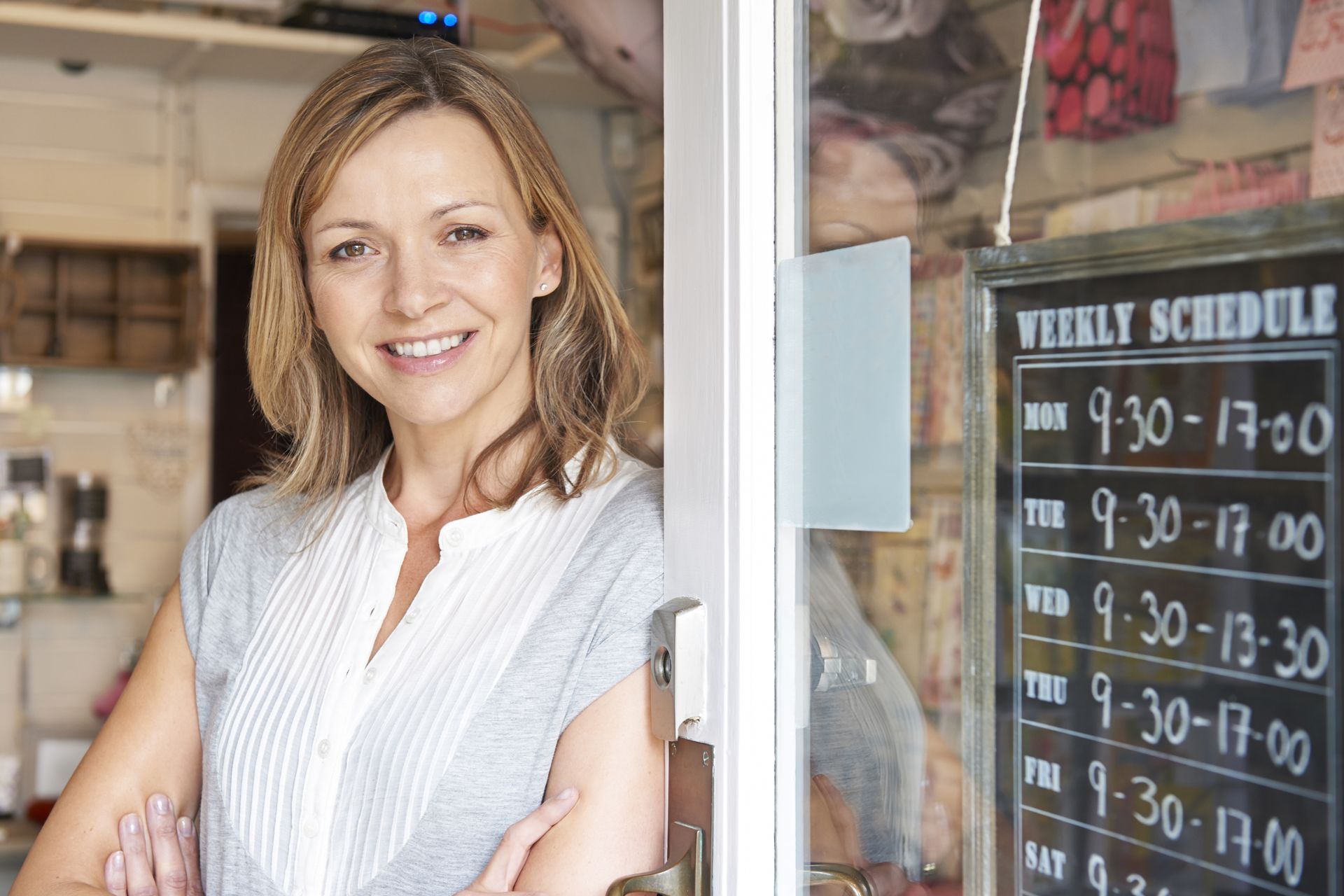 A woman is standing in front of a store door with her arms crossed.