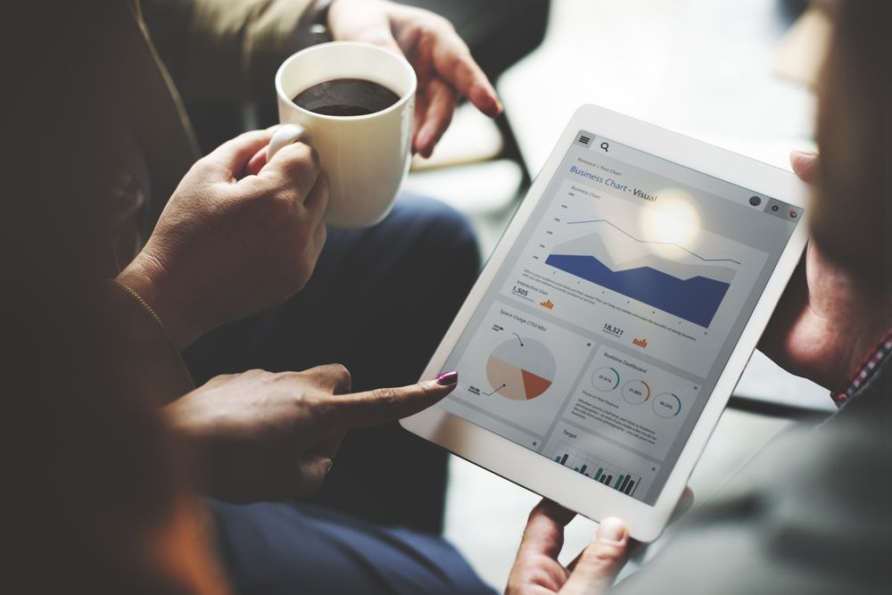 A man and a woman are looking at a tablet while holding a cup of coffee.