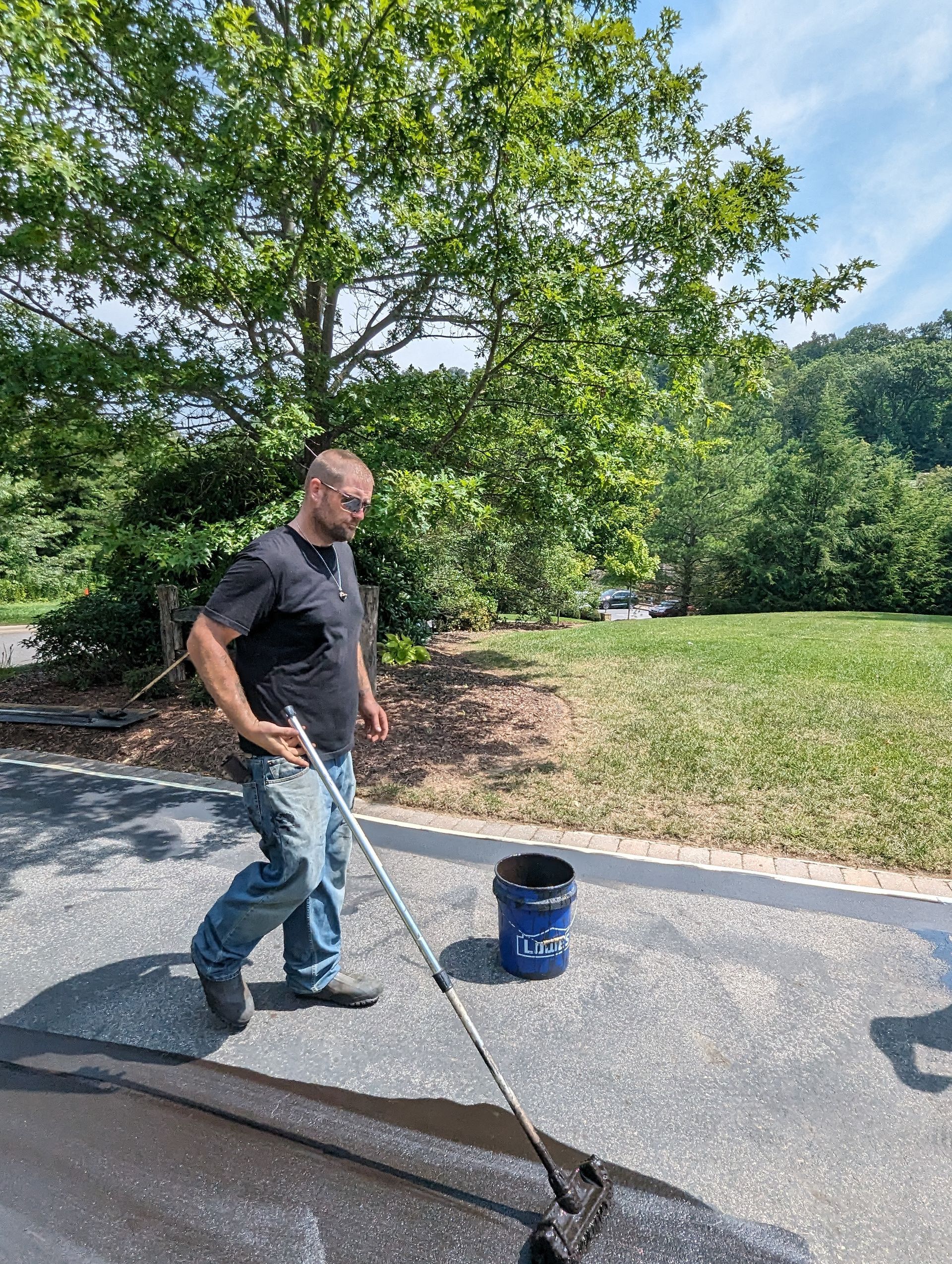 A man is spreading asphalt on a driveway with a broom.