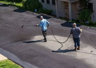 Two men are cleaning a driveway with a pressure washer.