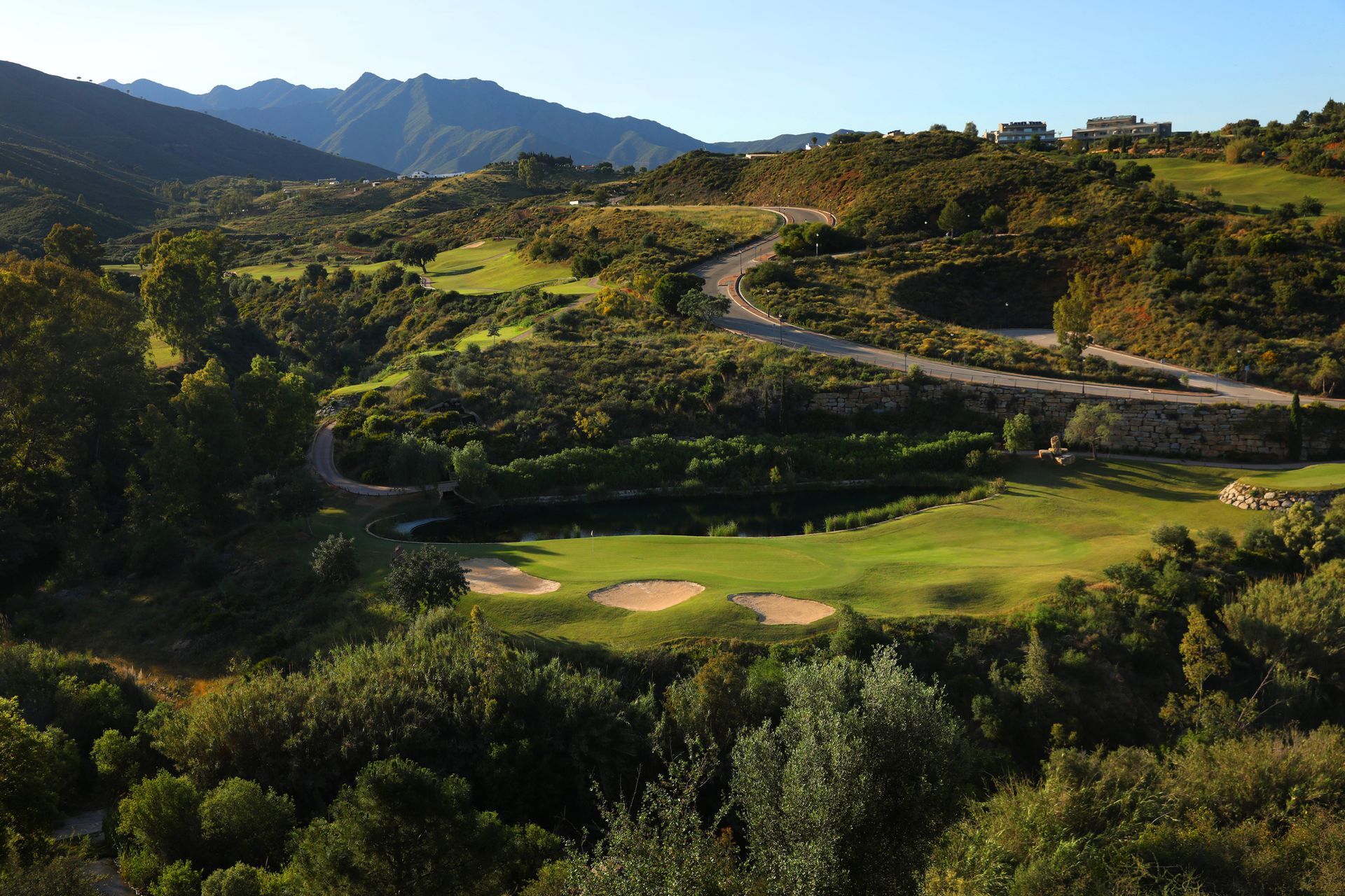Parcours de golf pittoresque niché dans une vallée avec des allées vertes, des fosses de sable et des collines environnantes.