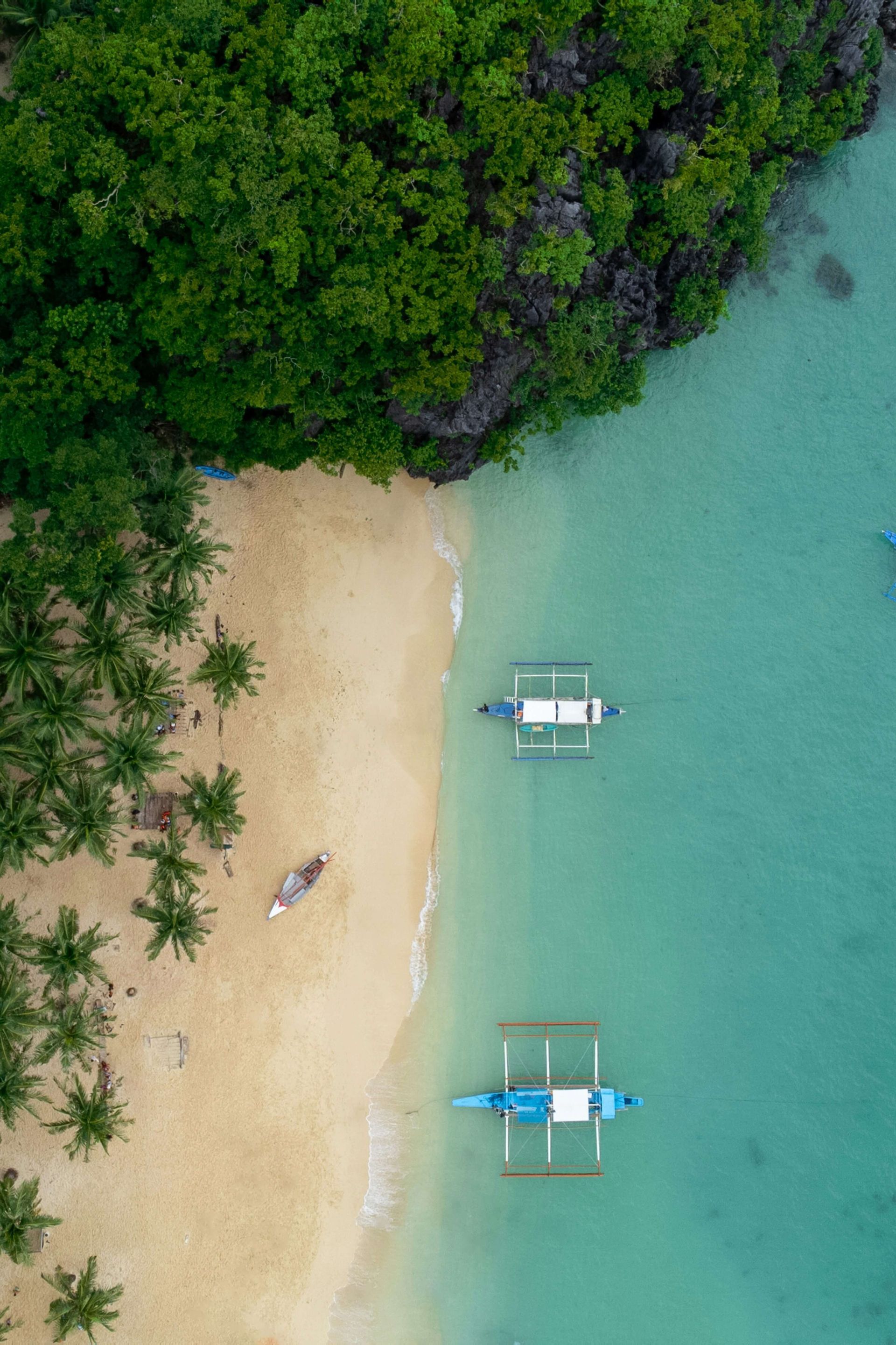 Vue aérienne d'une plage de sable fin aux eaux turquoise. Plusieurs bateaux flottent près du rivage