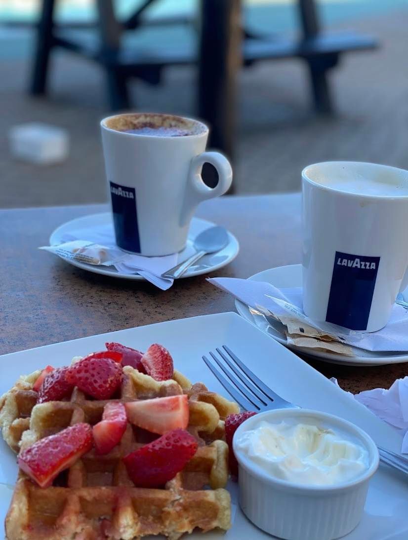 A waffle with strawberries and whipped cream next to two cups of lavazza coffee