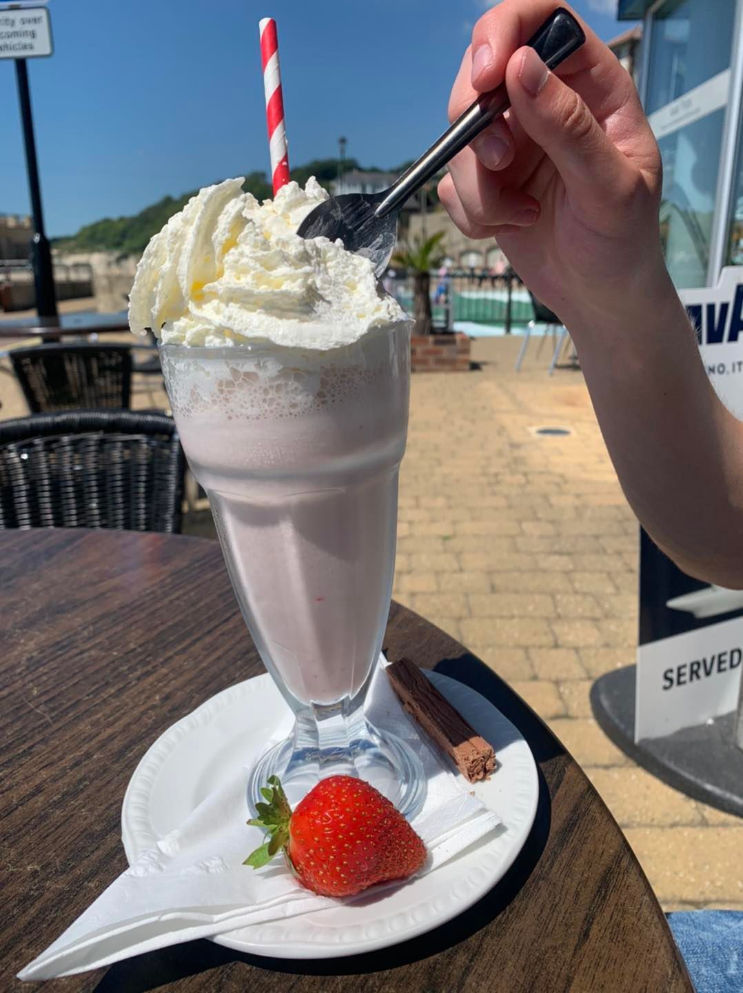 A person is drinking a milkshake with whipped cream and strawberries