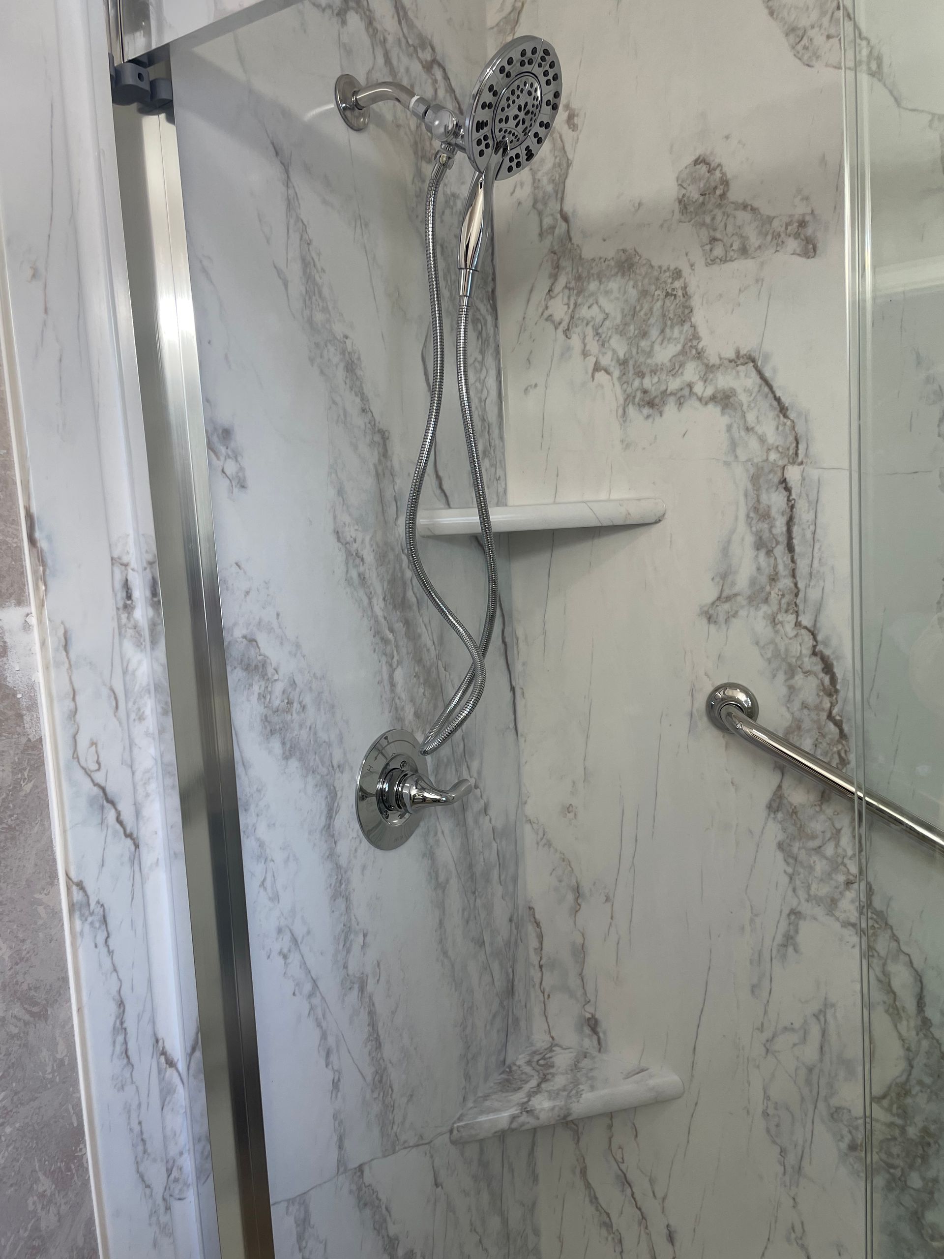A shower with a marble wall and a shower head.
