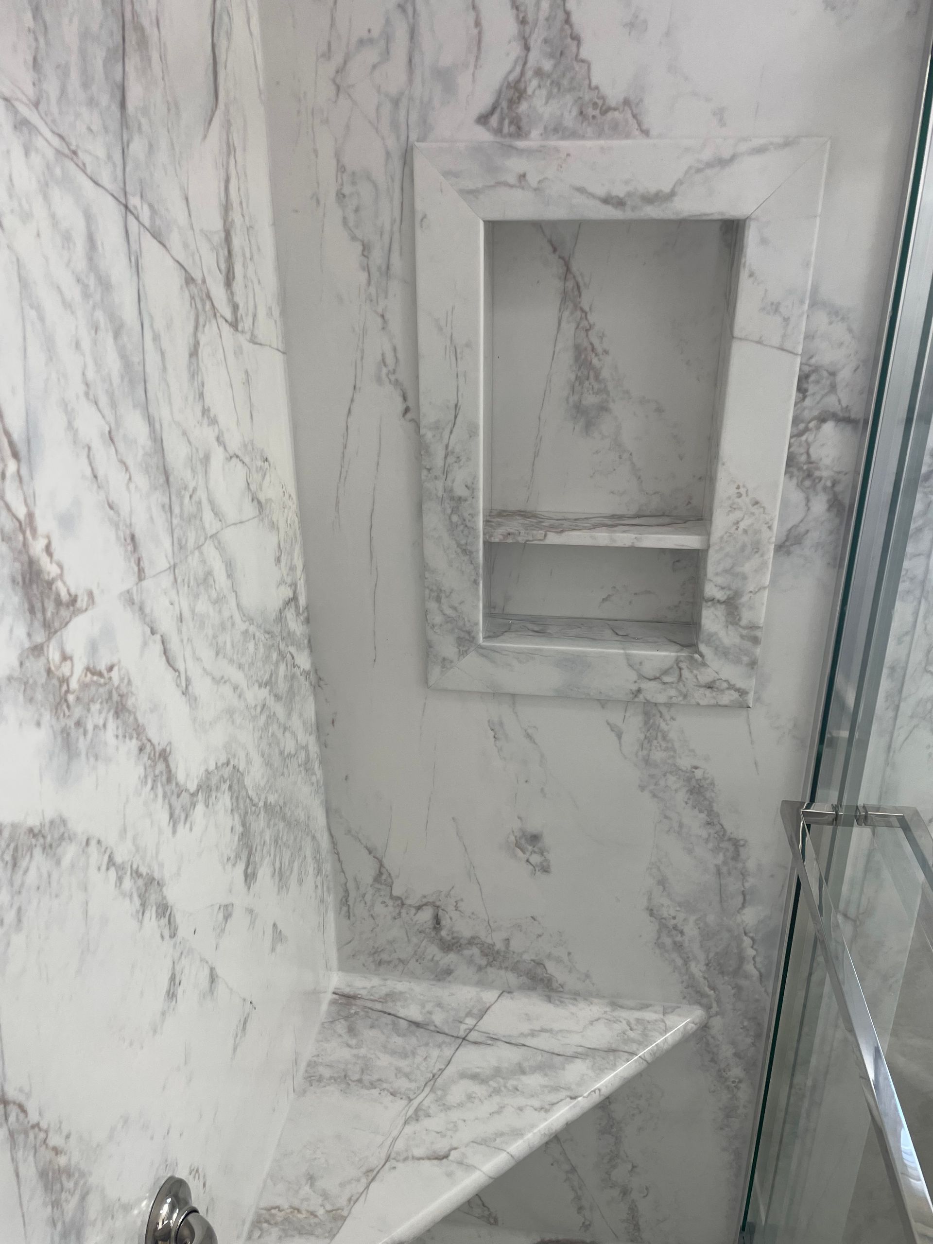 A bathroom with marble walls and a shelf in the shower.