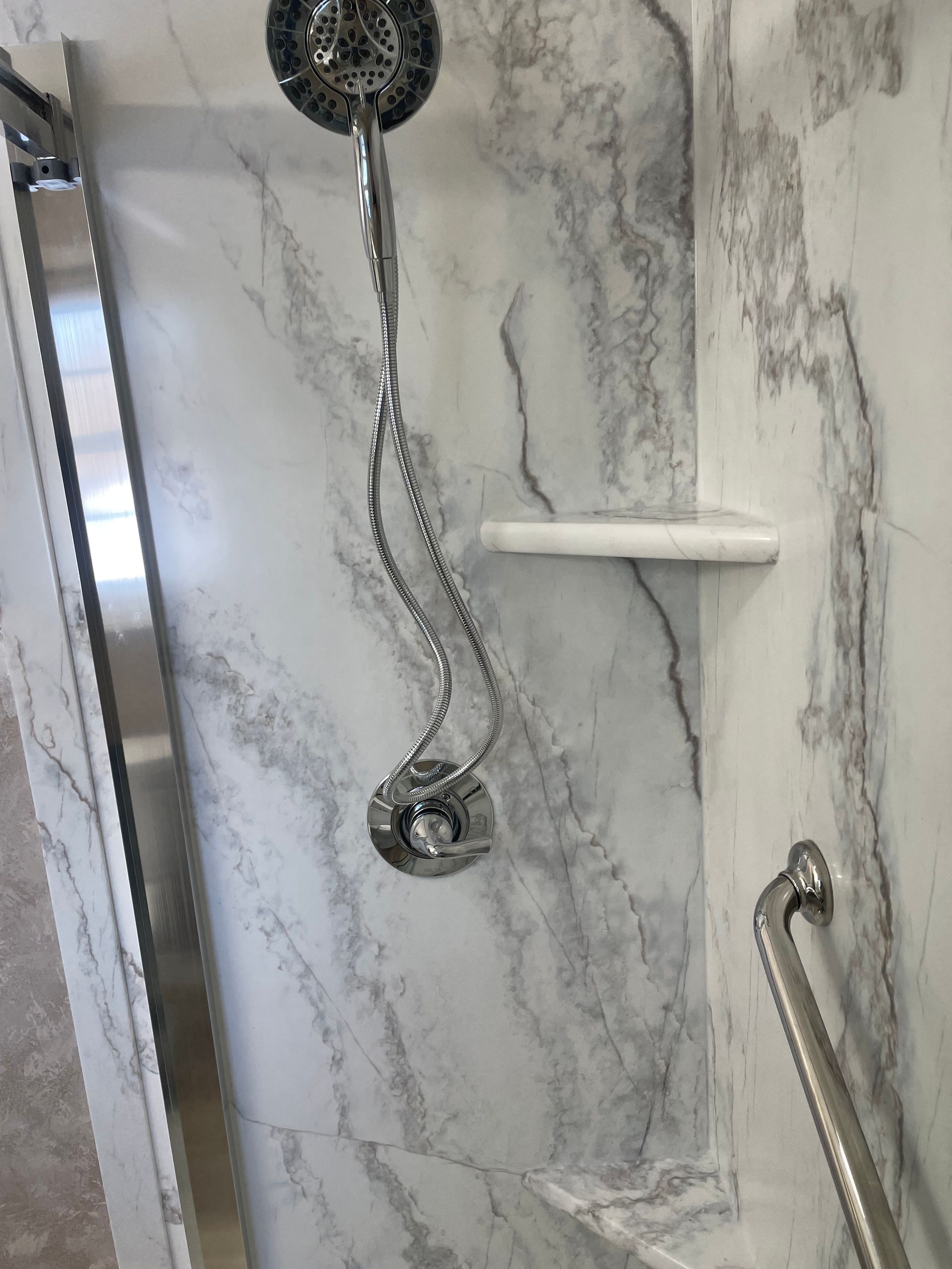 A shower head is hanging from a marble wall in a bathroom.