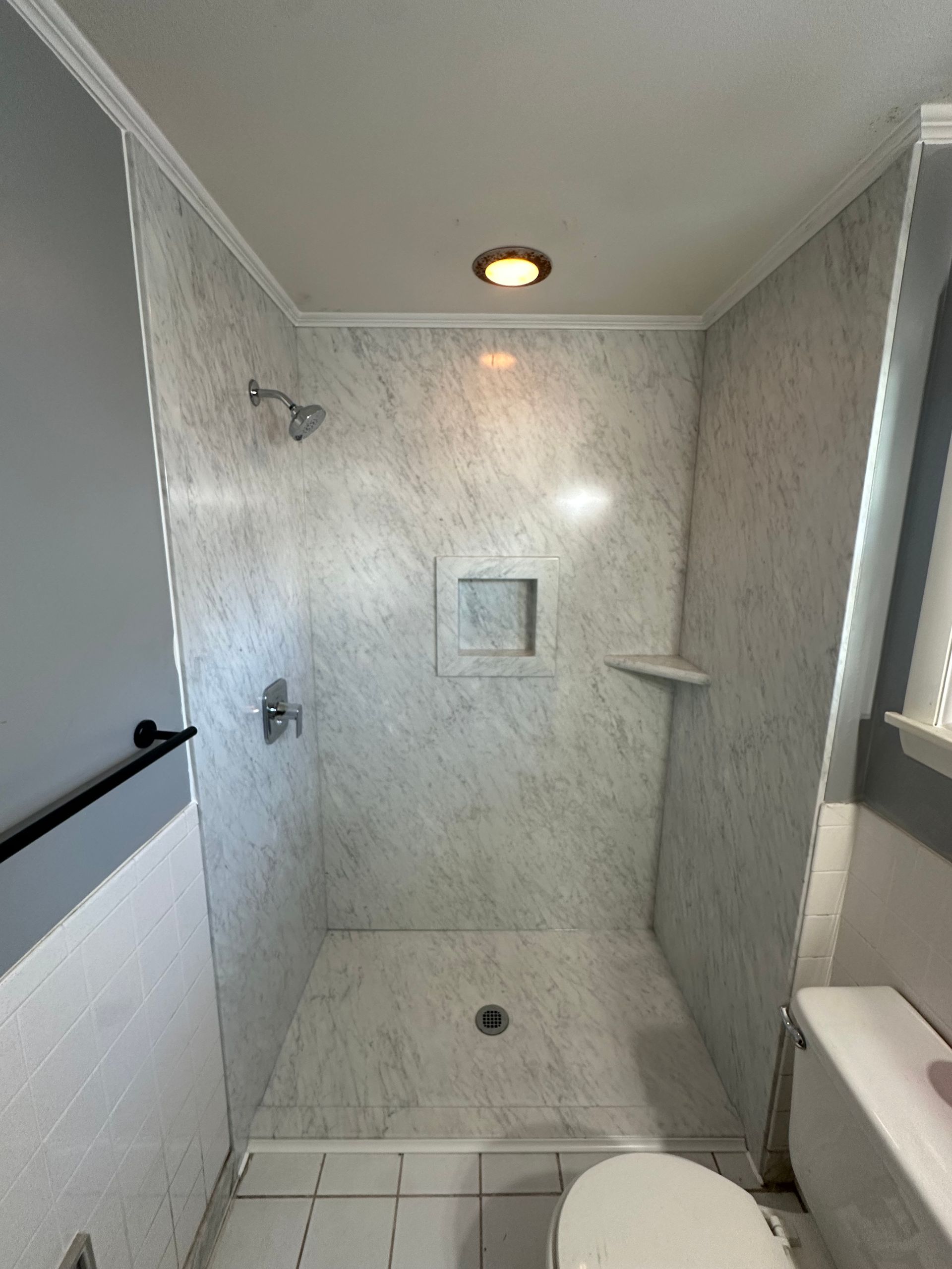 A bathroom with a toilet , shower , and window.