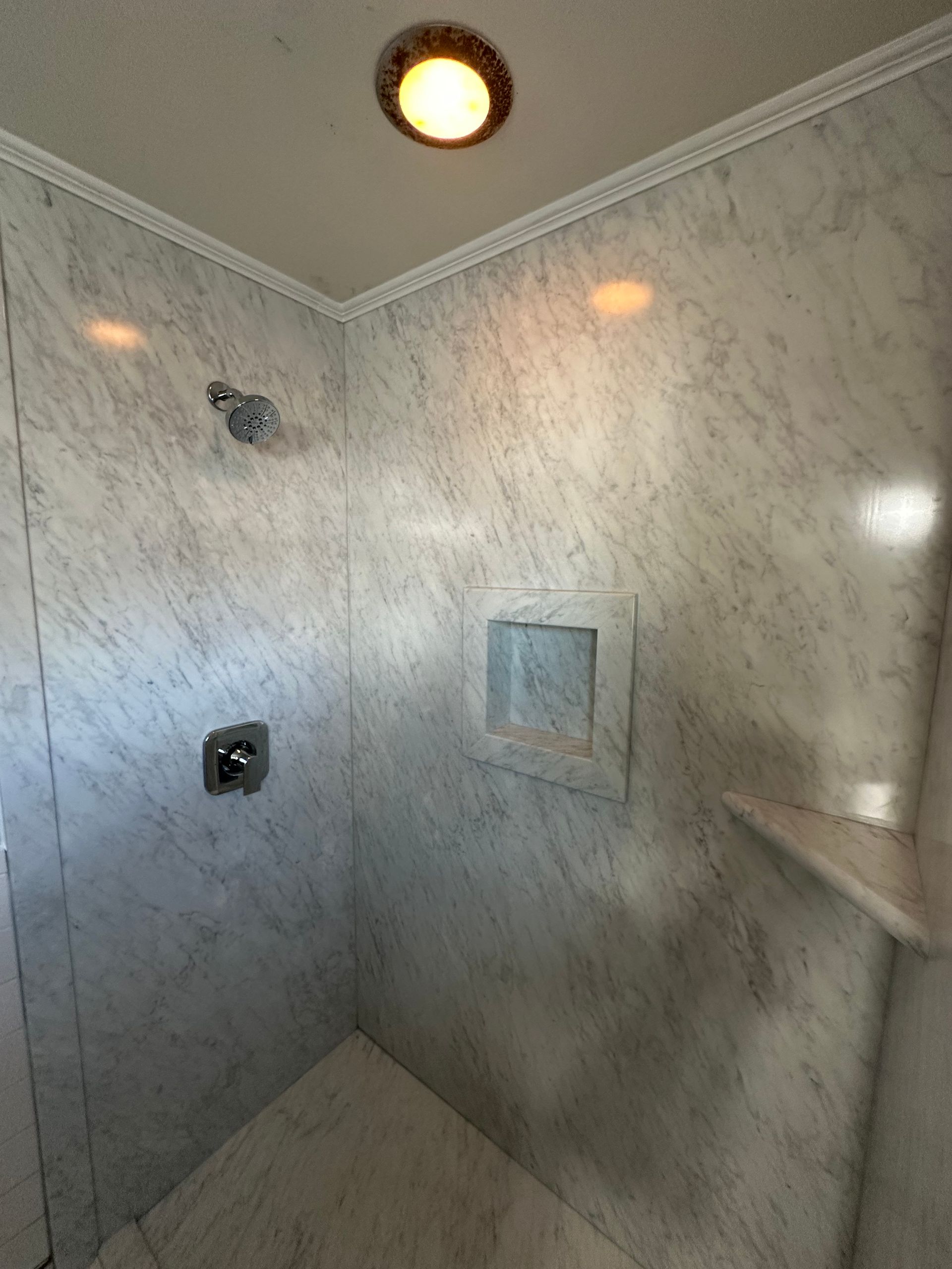 A bathroom with marble walls and a walk in shower.
