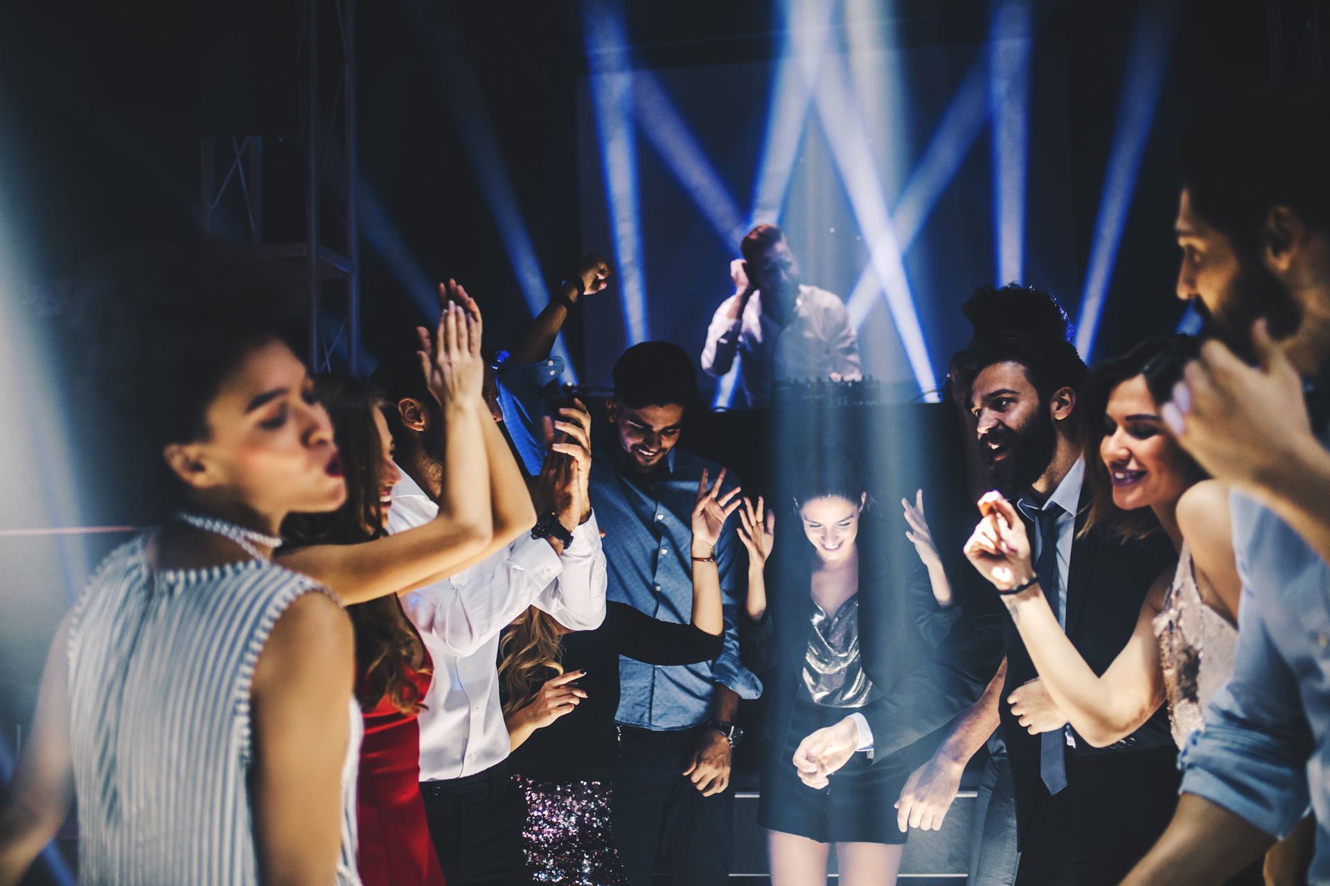People dancing in a nightclub under spotlights, hands raised in the air.
