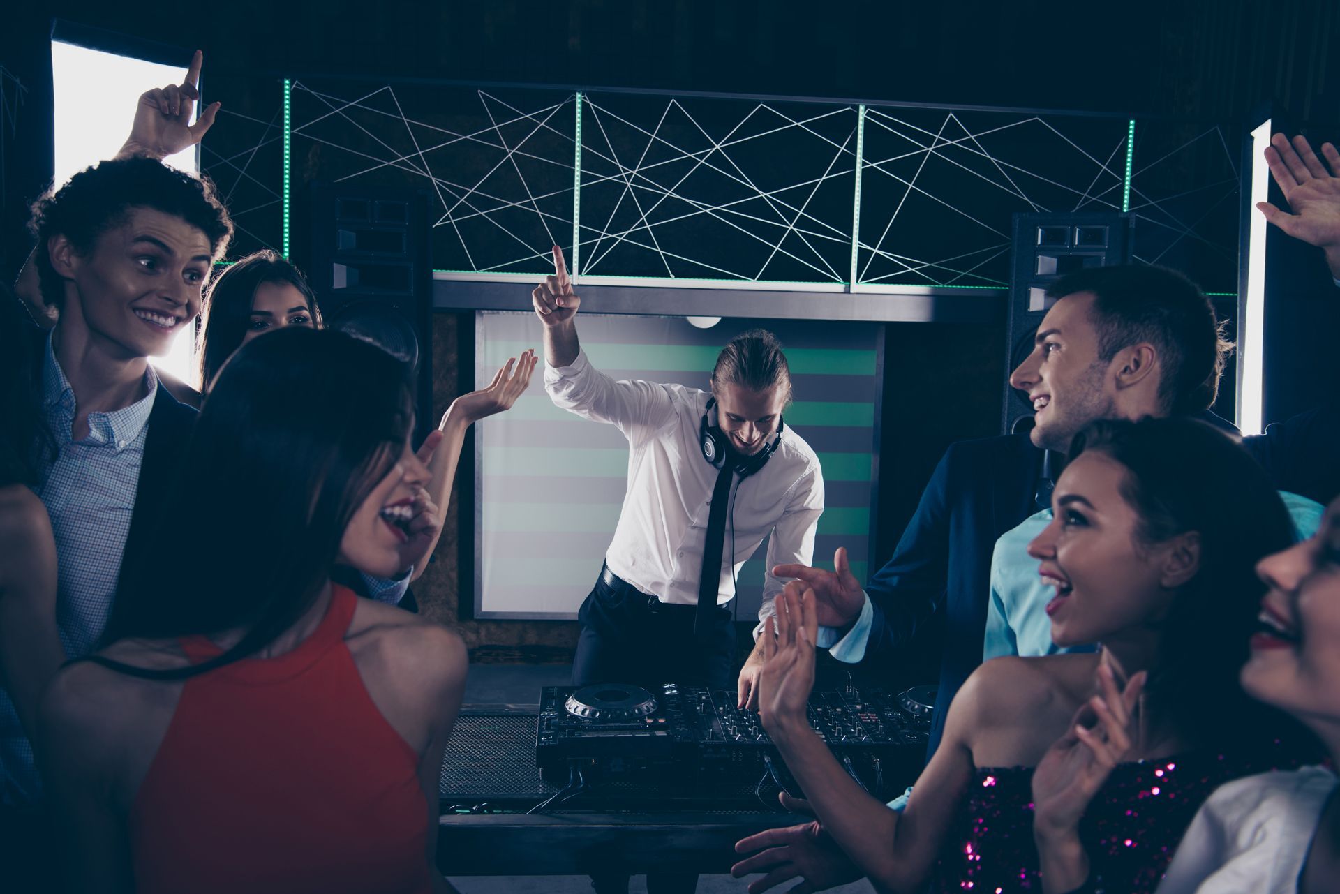 People dancing at a club, DJ with arms raised, blue and white lights.