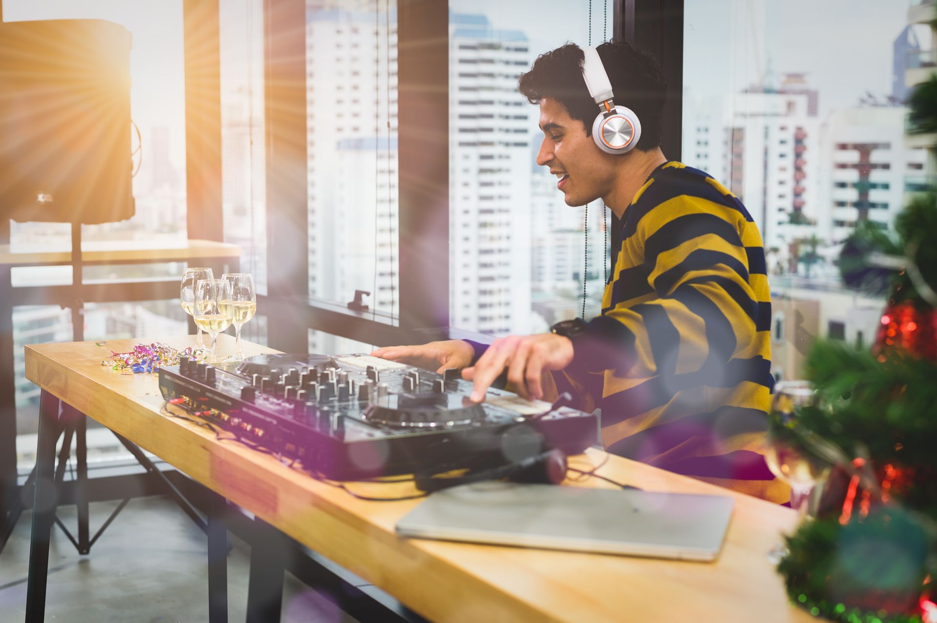 Man at DJ setup, smiling, with headphones on, near window, inside.