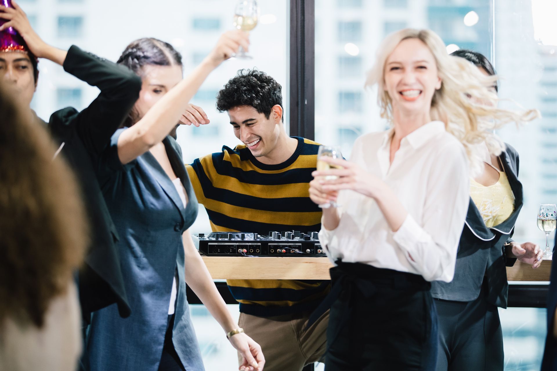 Office workers celebrate, some with drinks, near a window. 