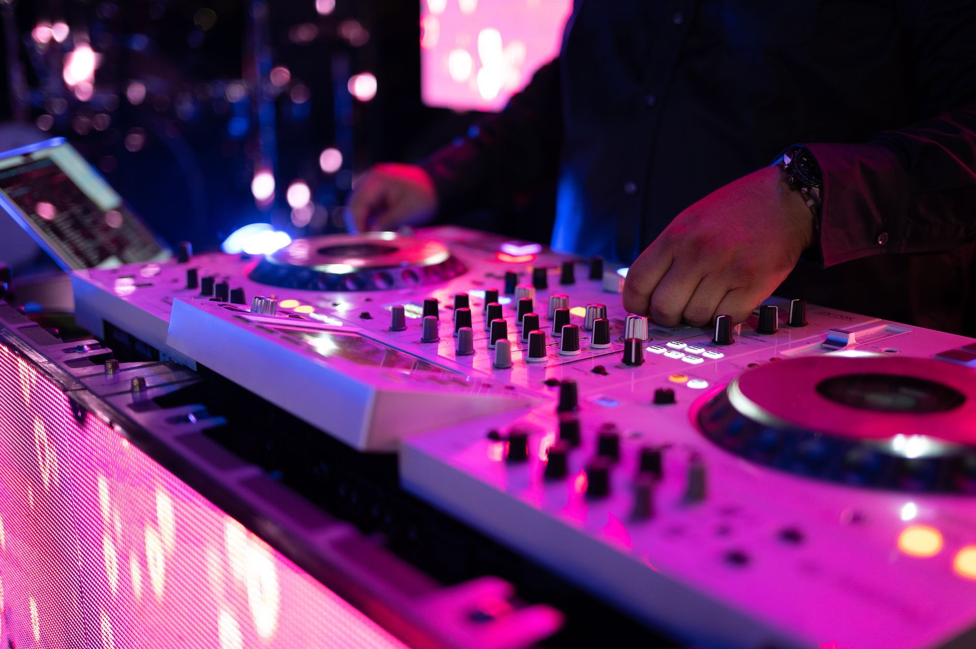 DJ mixing music on a white soundboard with pink and blue lights.