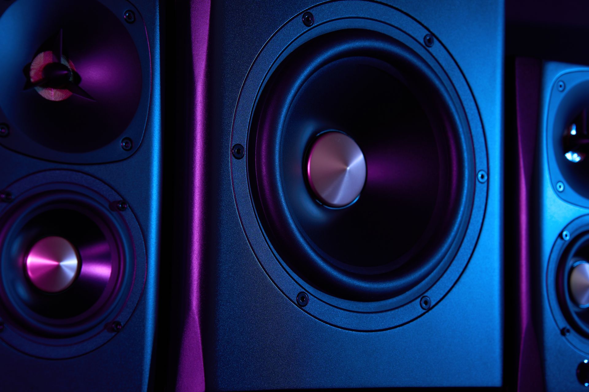 Three studio monitor speakers with black drivers, lit by blue and purple light.
