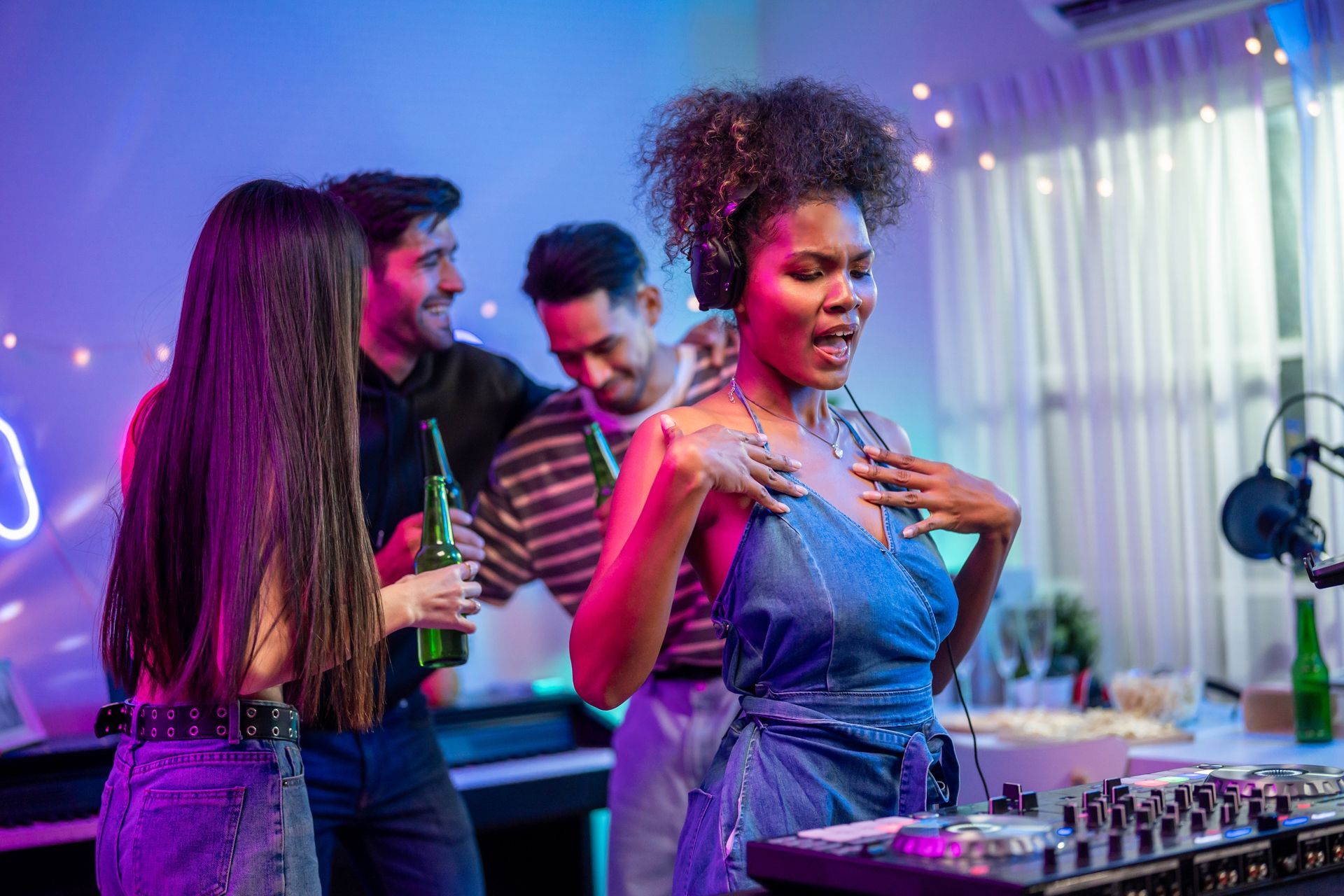 People at a party with DJ equipment, neon lights, and a woman singing into a microphone.