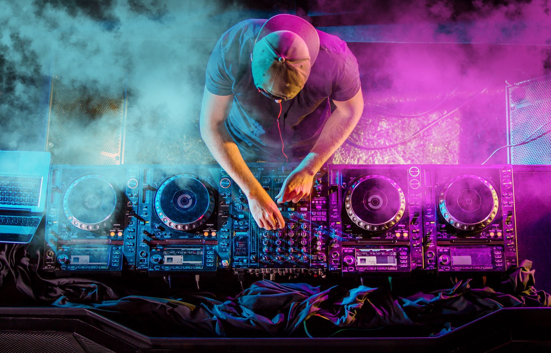 DJ at a console mixing music with blue and pink lighting and smoke.