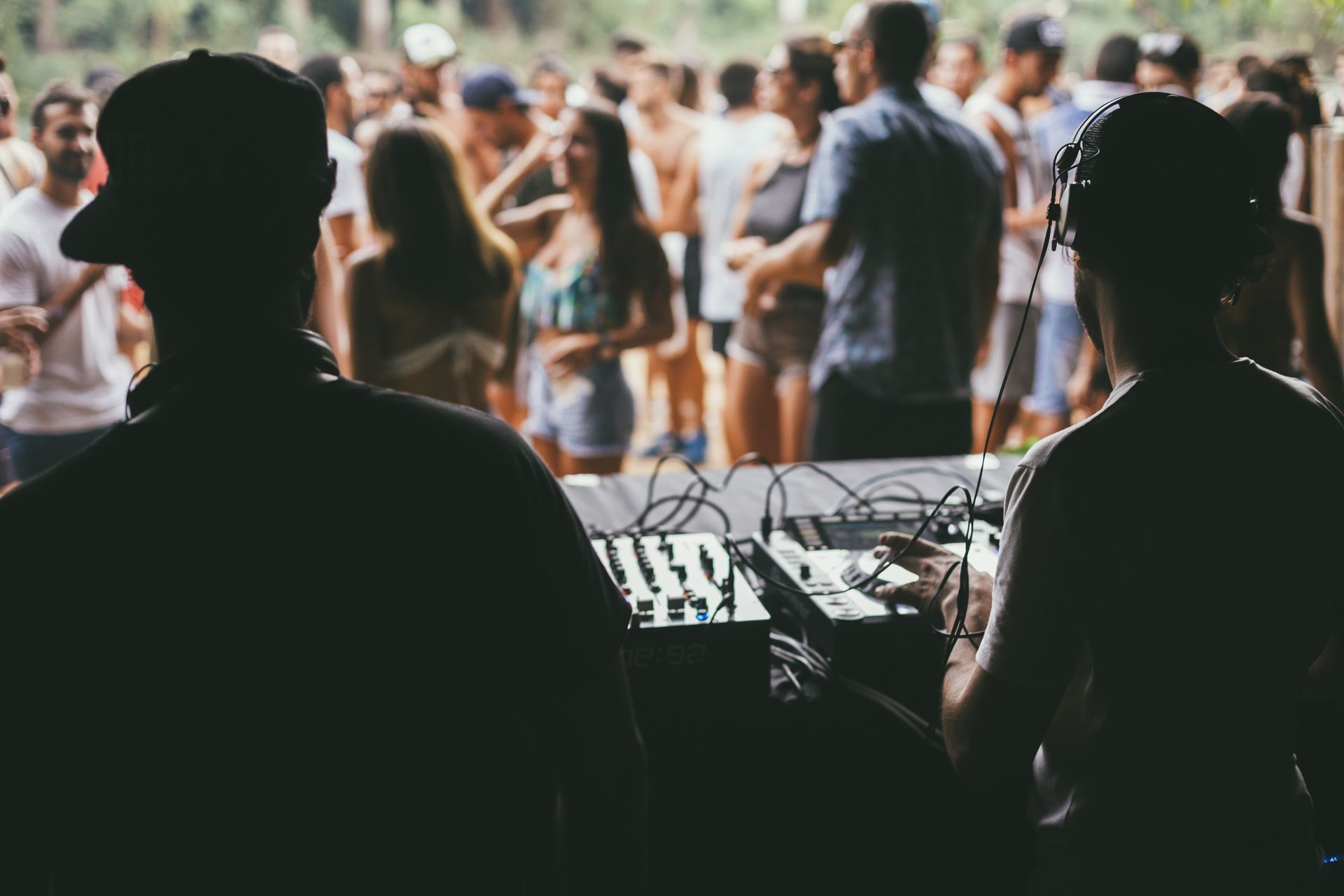 Two DJs at a music festival, silhouetted against a crowd of people.