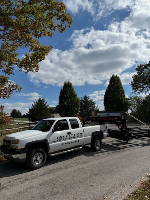 White truck with trailer parked on a road, trees and cloudy sky in the background. Truck has 