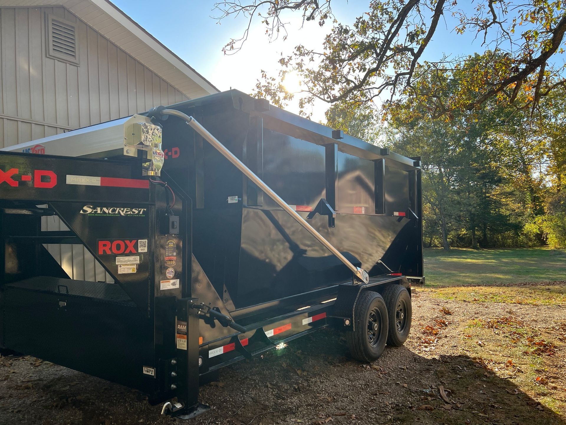 Black dump trailer parked outdoors, near a building and trees.