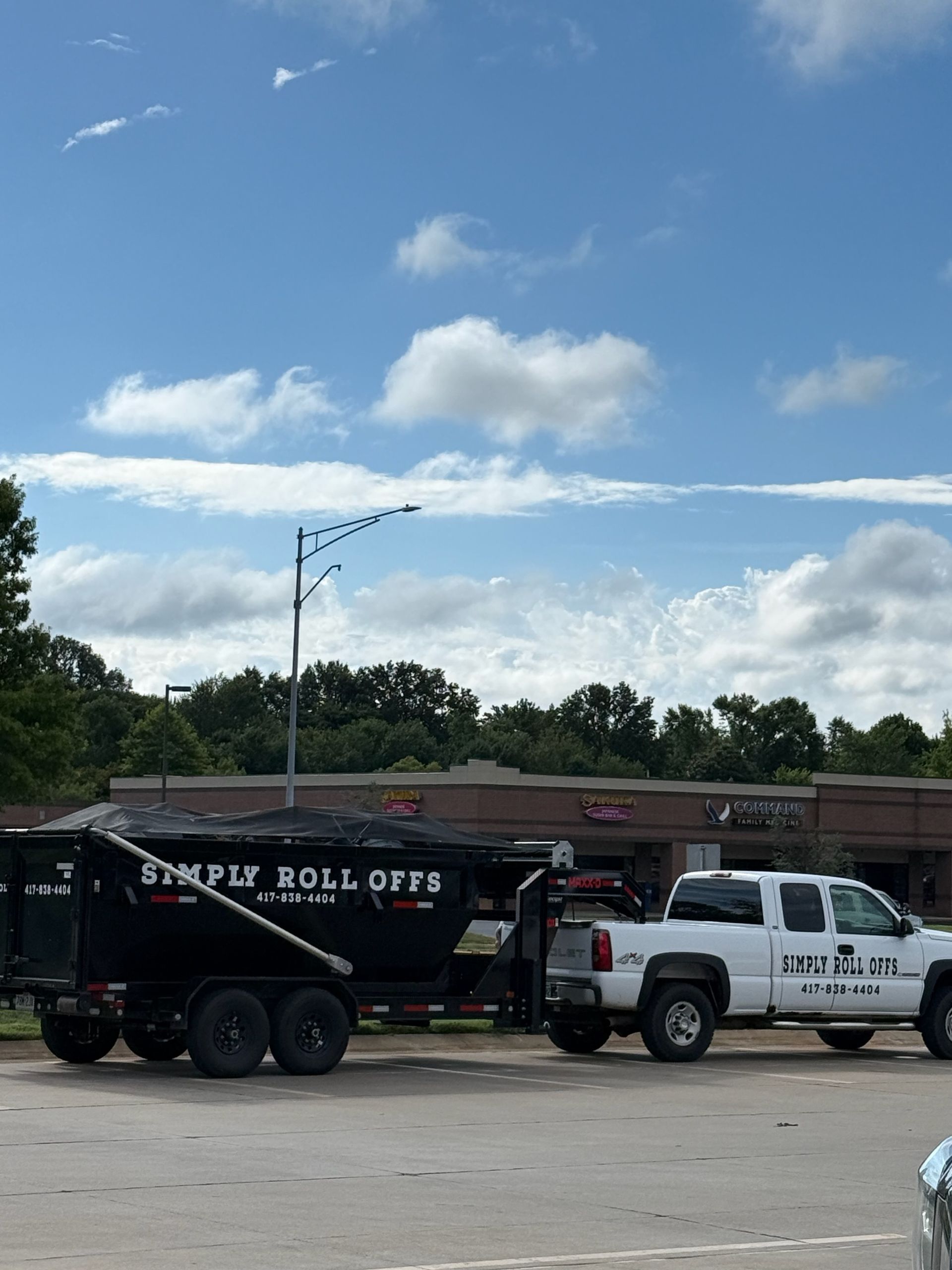 White truck towing a black dumpster trailer with 