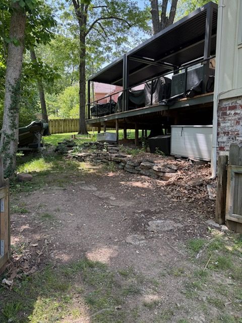 Wooded backyard with dirt path, trees, and a raised screened porch on the right.