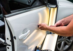 A man is repairing a car door with a light.