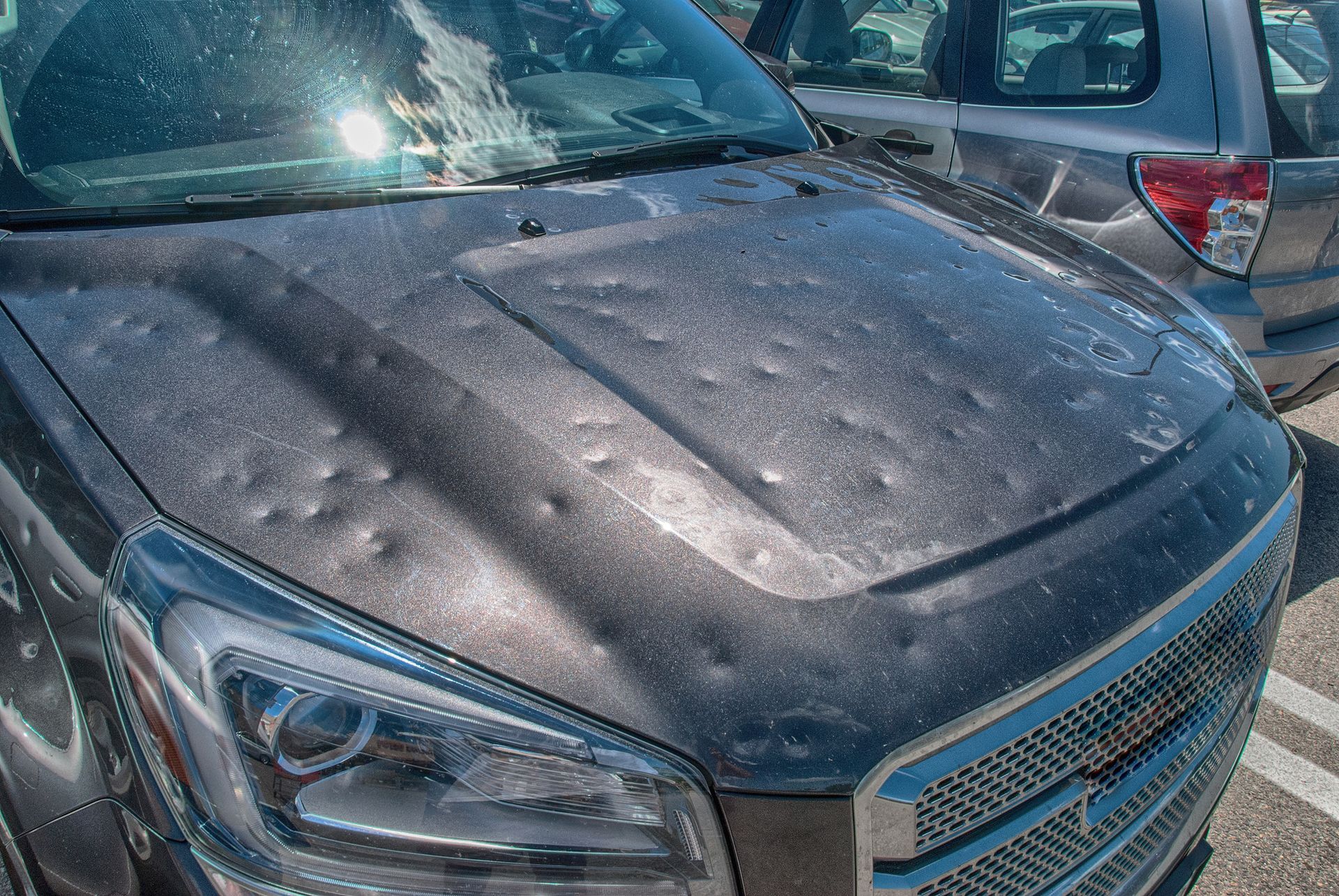 A car with hail damage on the hood is parked in a parking lot.