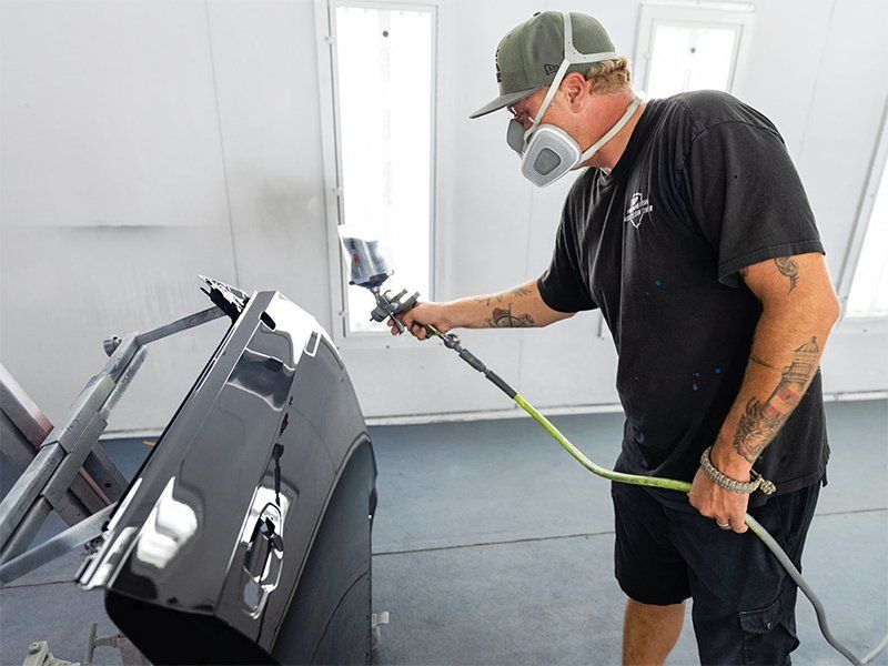 A man wearing a mask is spray painting a car