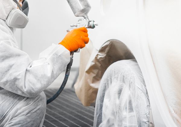 A man in a protective suit is spray painting a car.