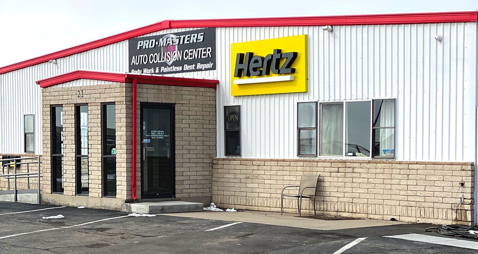 A white building with a yellow sign that says hertz on it.